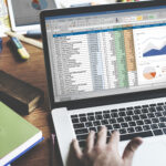 Closeup of hands using computer laptop with screen showing analysis data
